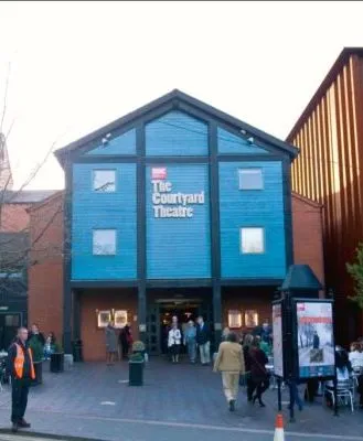 Front view of the Courtyard Theatre in Stratford-upon-Avon, with people gathering outside the entrance on a lively day, and the building's distinctive blue facade.