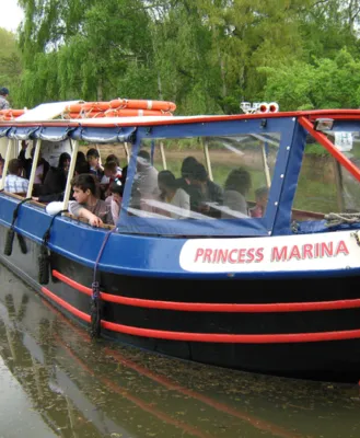 Blue and red riverboat named 'Princess Marina' filled with passengers, cruising along a calm, tree-lined river, with greenery visible in the background.