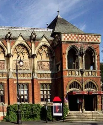 Exterior of the historic Swan Theatre in Stratford-upon-Avon, showcasing its ornate Gothic-style architecture with pointed arches, decorative stonework, and a red telephone booth nearby.