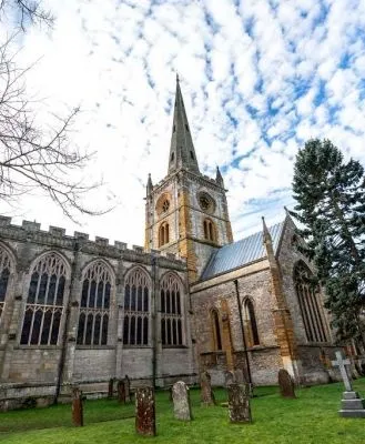 Gothic-style church with tall spire and arched stained-glass windows, surrounded by a historic cemetery under a partly cloudy sky.