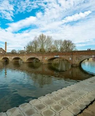 Historic Tramway Bridge in Stratford-upon-Avon, spanning over a calm river under a bright blue sky with scattered clouds.