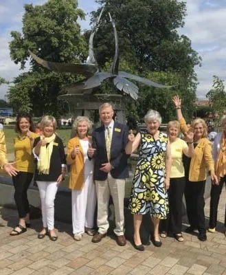 Group of friendly town walk guides in bright yellow attire posing in front of a sculpture in Stratford-upon-Avon on a sunny day.