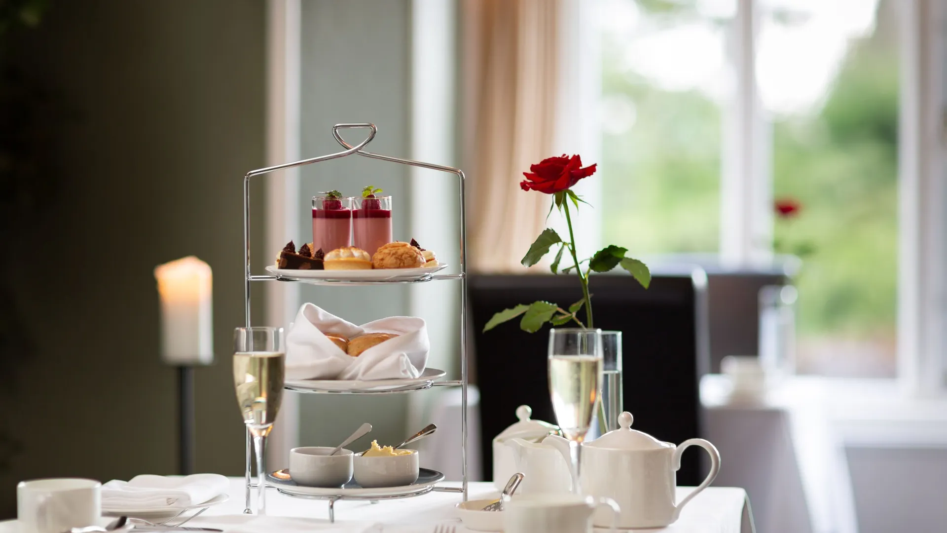 Elegant afternoon tea set with pastries, scones, tea, and a single red rose on a white tablecloth