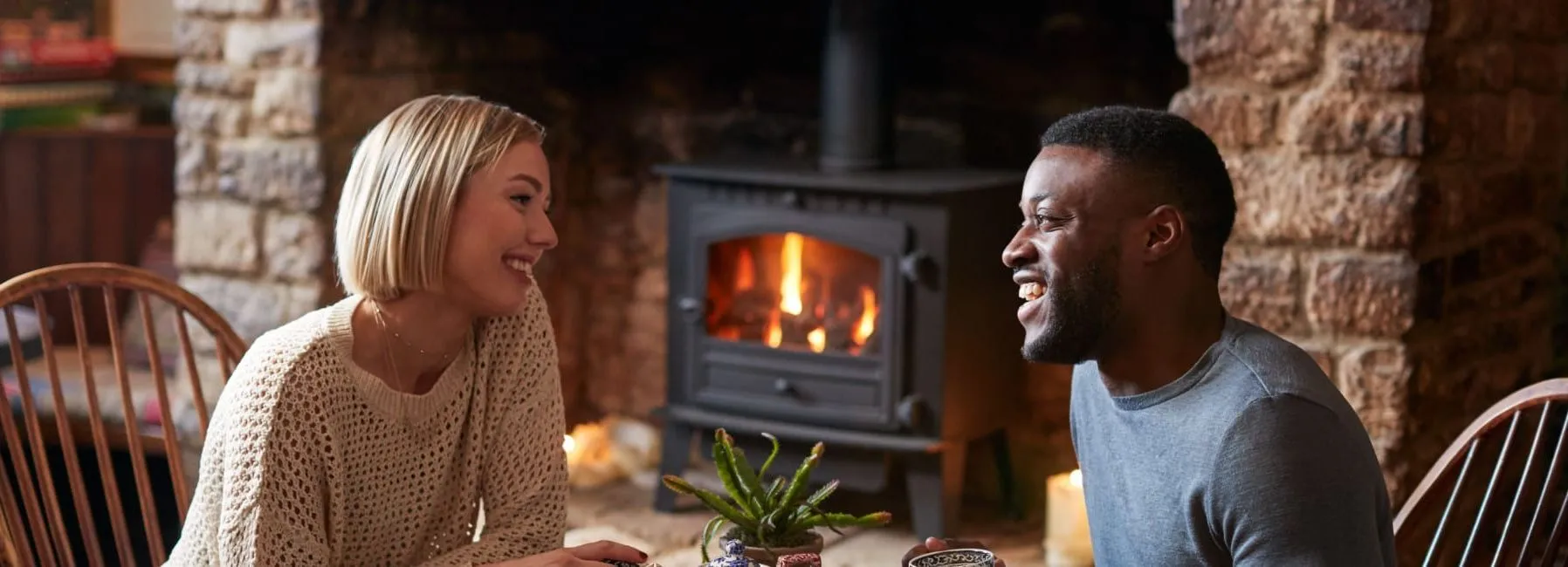 Couple smiling and enjoying coffee together by a fireplace in a cozy rustic setting