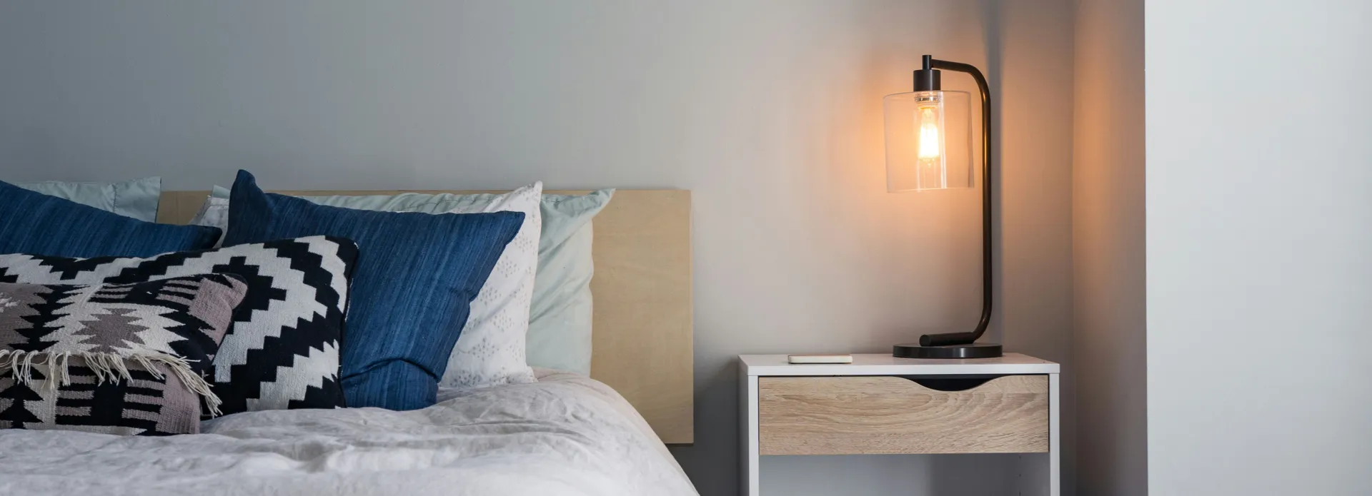 Modern bedroom with blue and white bedding, a geometric pillow, and a lit bedside lamp on a nightstand
