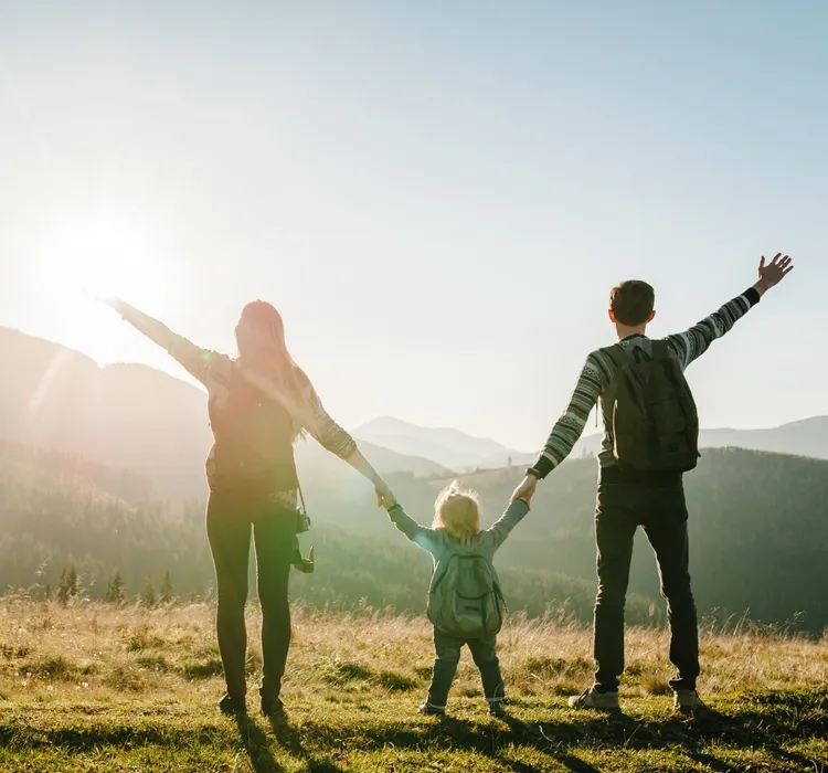 Family with backpacks enjoying a scenic view in the mountains at sunrise.