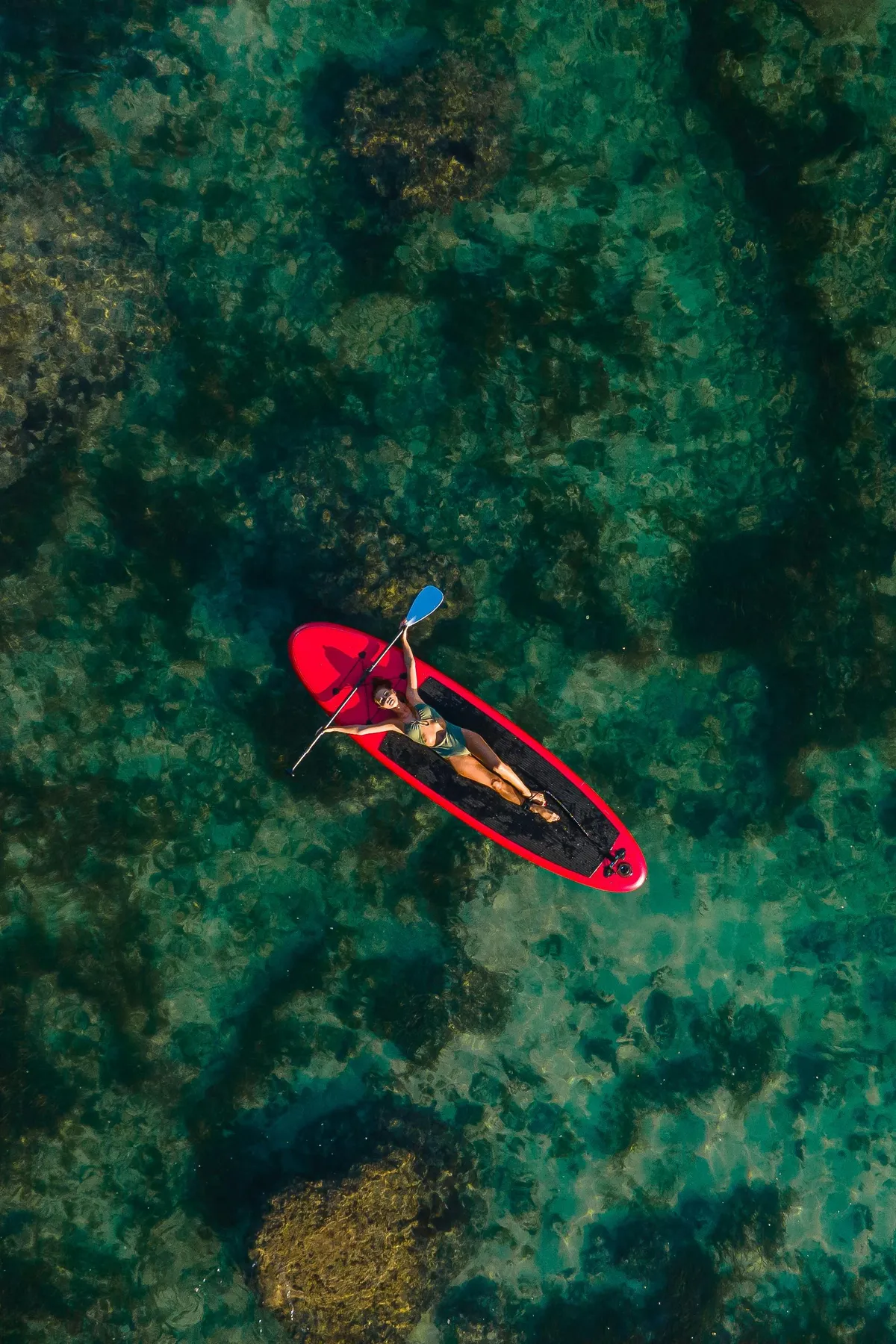 Person paddling a red kayak in clear turquoise water seen from above