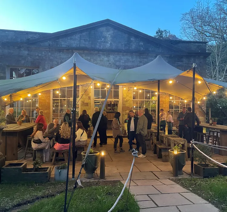 Outdoor gathering under a canopy with string lights in front of a stone building