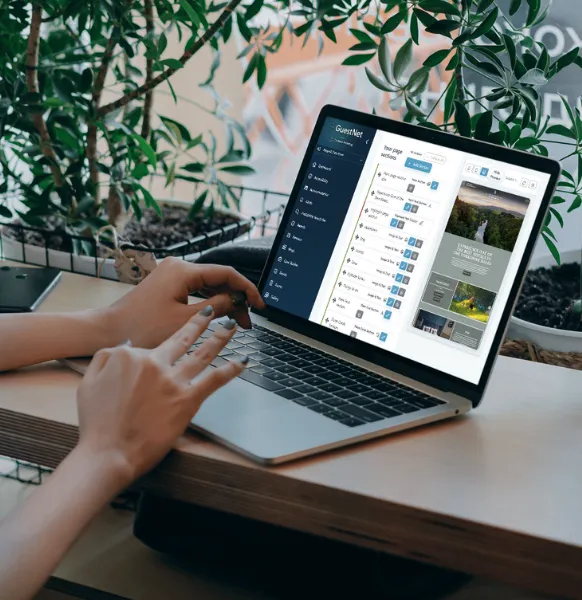 Person using a laptop displaying the GuestNet dashboard interface at a desk surrounded by plants.