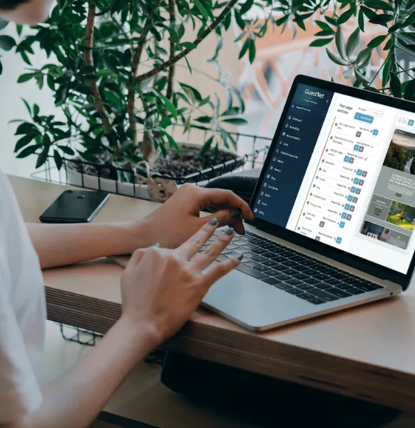Person using a laptop displaying the GuestNet dashboard interface at a desk surrounded by plants.