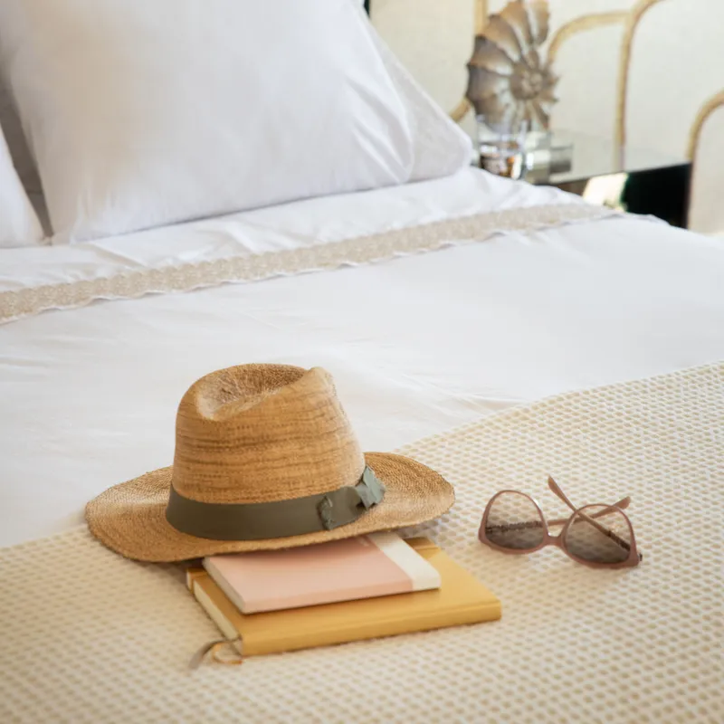 Straw hat, sunglasses, and books on a neatly made bed