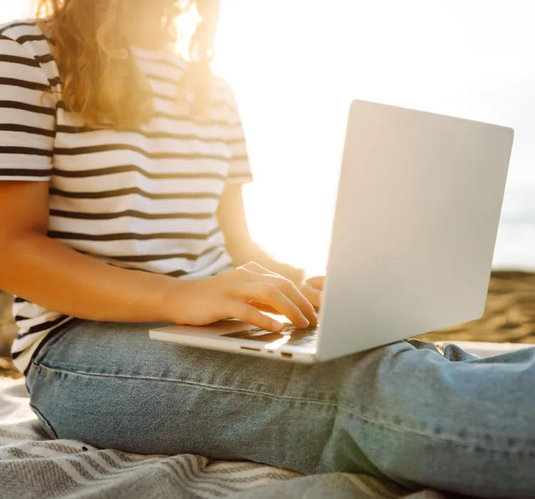 Person sitting on beach using a laptop