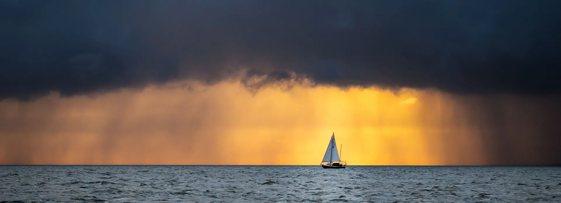 Sailboat on the ocean with dramatic clouds and golden sunset in the background