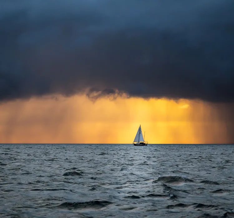 Sailboat on the ocean with dramatic clouds and golden sunset in the background