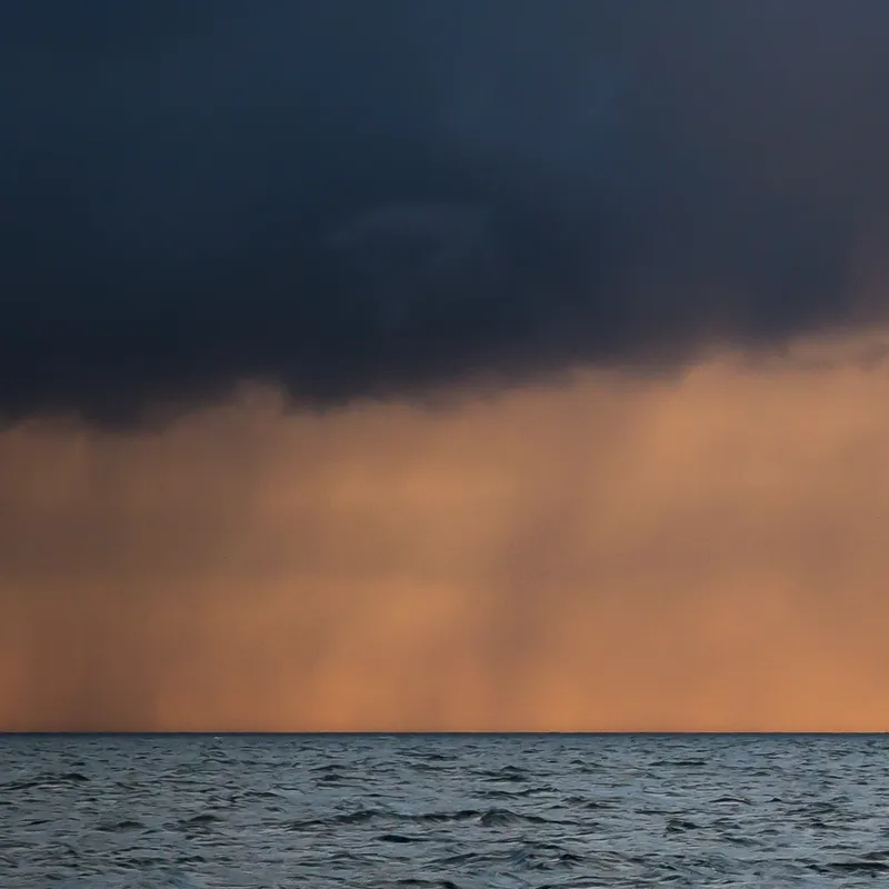 Dark storm clouds over a calm sea with orange light on the horizon