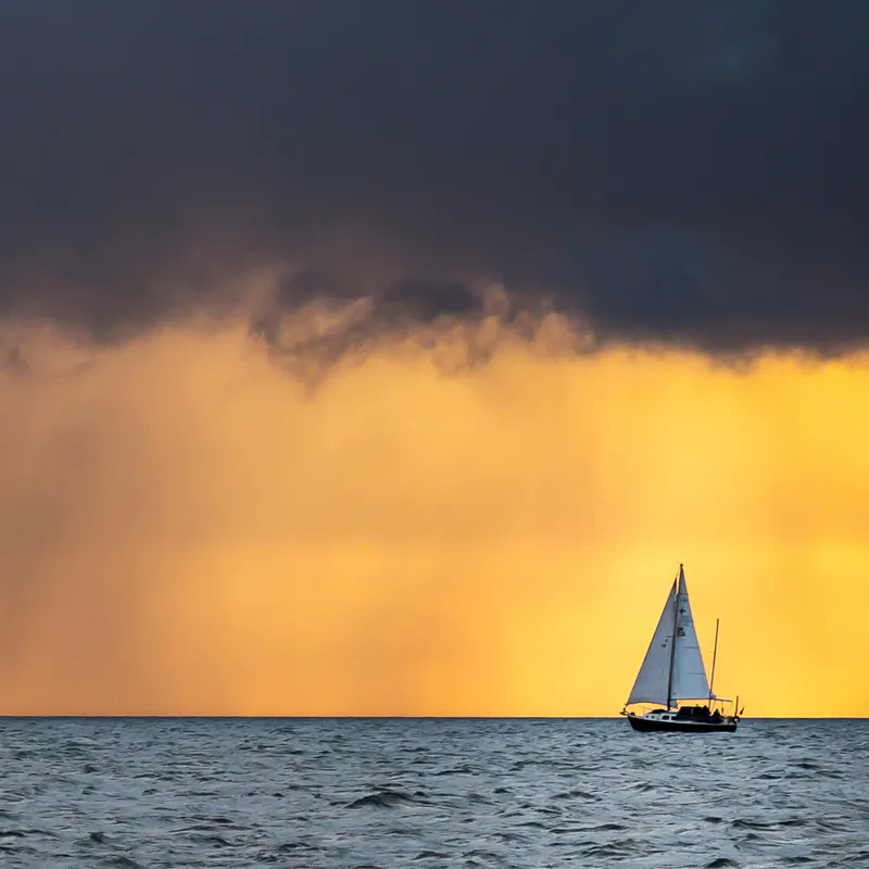 Sailboat on the ocean with dramatic yellow and dark clouds at sunset