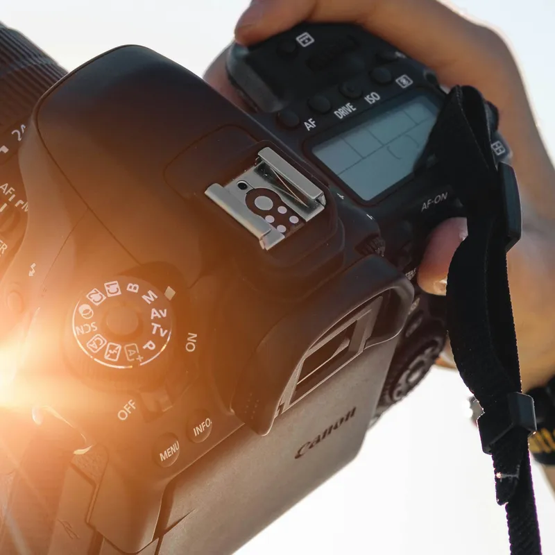 Person holding a DSLR camera with mode dial and control buttons visible.