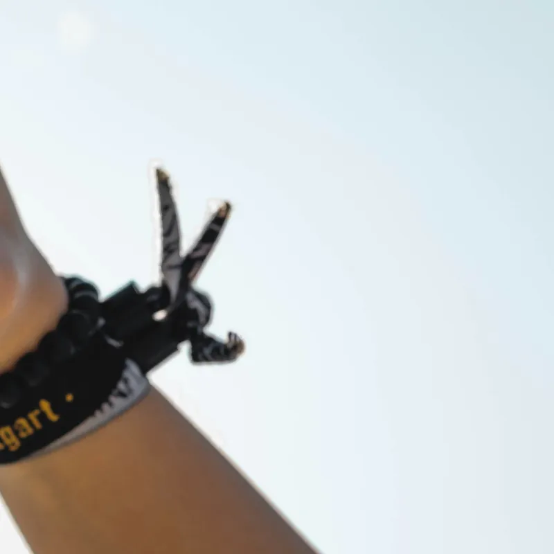 Hand making a peace sign against a clear sky, wearing a black wristband and bracelet.