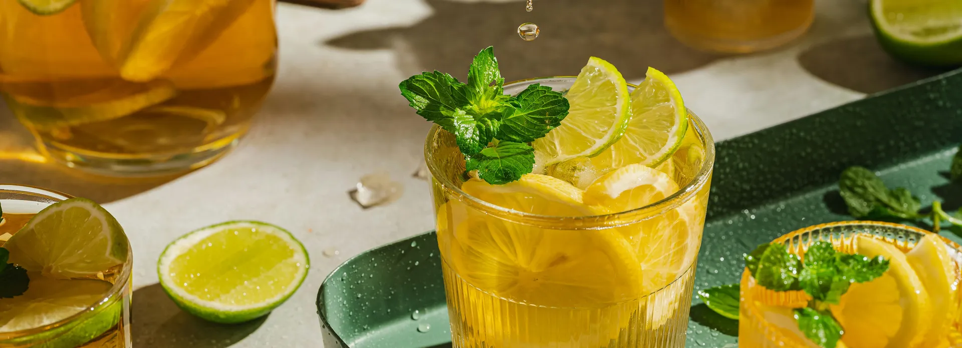 Glasses of iced lemon tea with fresh lemon and lime slices, garnished with mint leaves