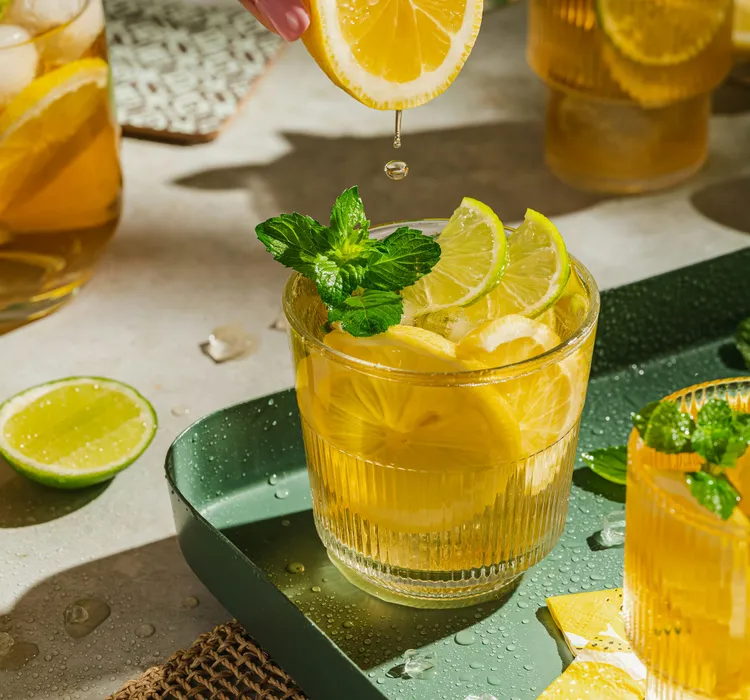 Glasses of iced lemon tea with fresh lemon and lime slices, garnished with mint leaves