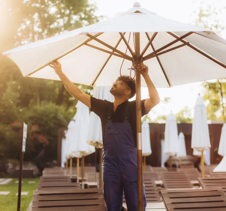 Man adjusting a large outdoor umbrella by the poolside