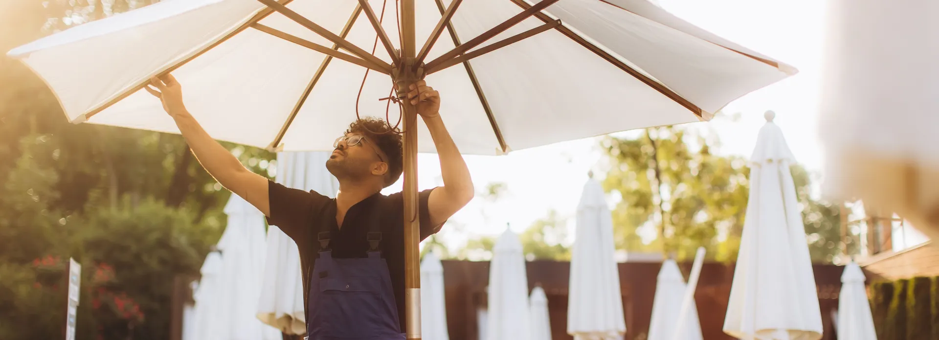 Man adjusting a large outdoor umbrella by the poolside