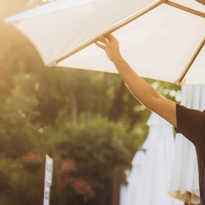 Person opening a large outdoor umbrella in a sunny garden setting