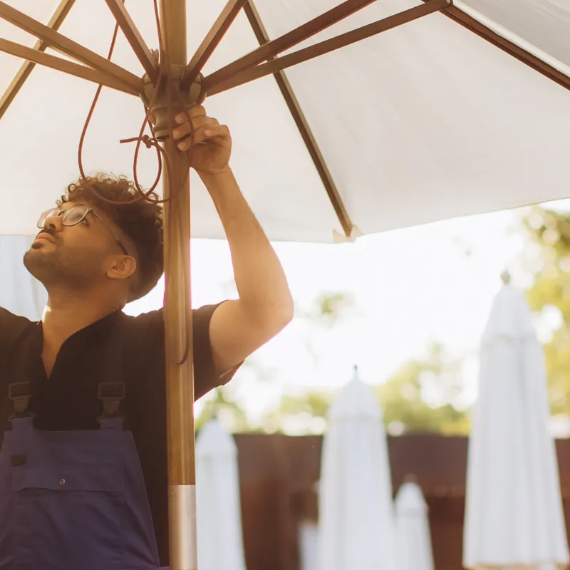 Person adjusting a large outdoor umbrella with several closed umbrellas in the background.