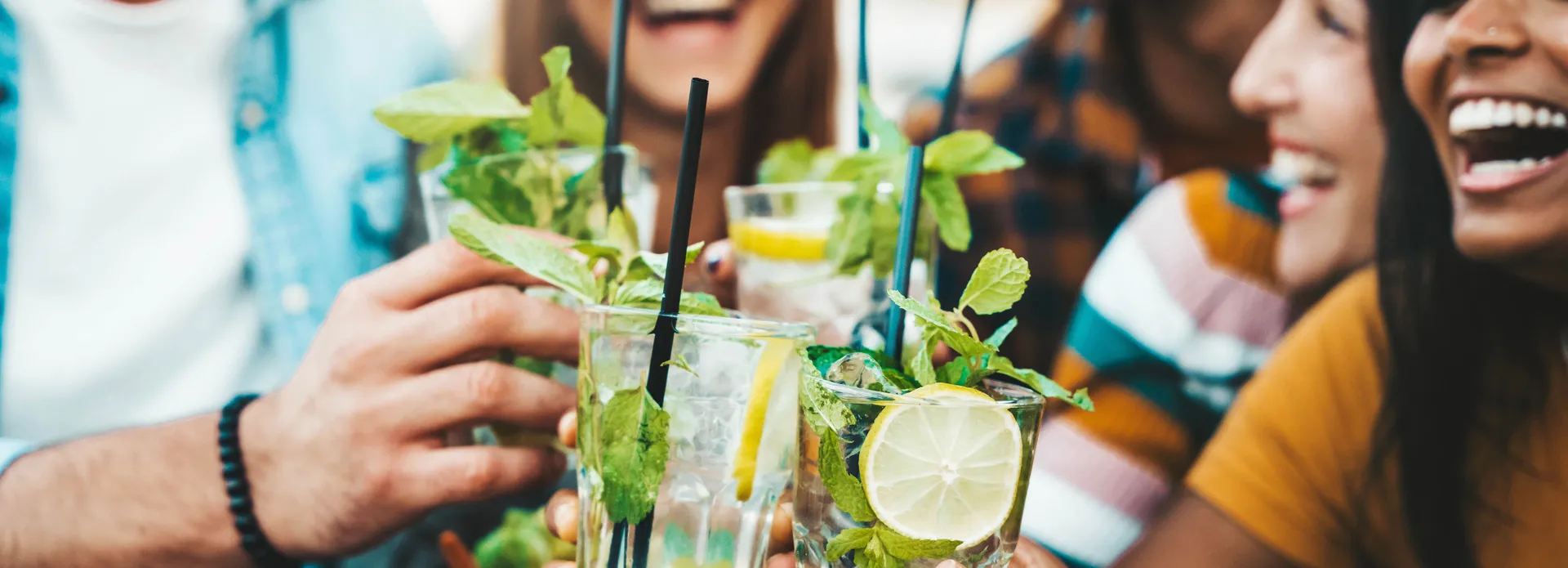 Group of friends clinking glasses with cocktails and smiling outdoors.