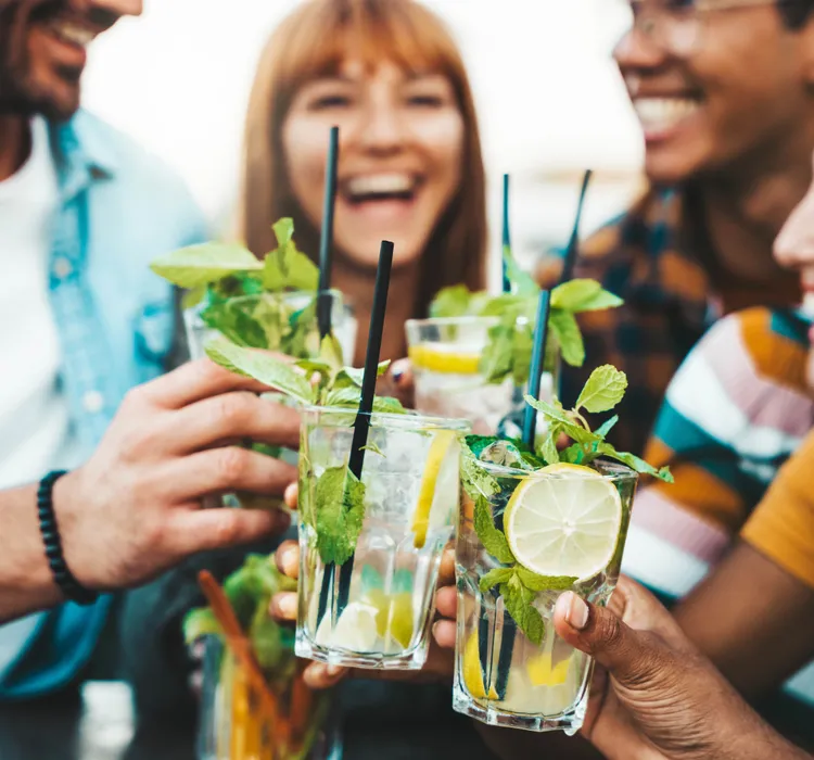 Group of friends clinking glasses with cocktails and smiling outdoors.