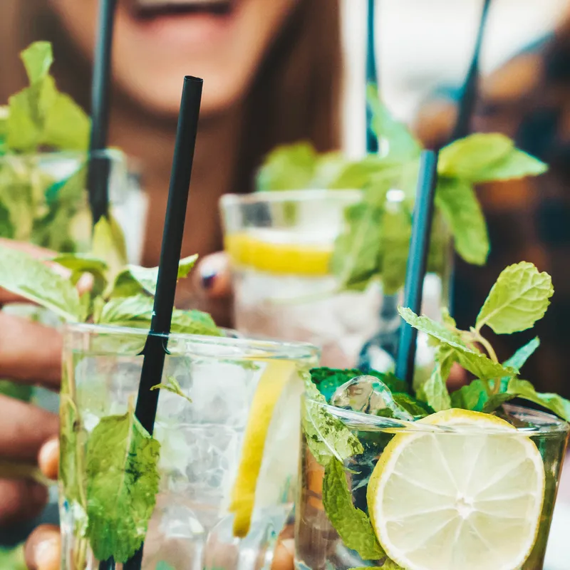 Close-up of people holding glasses of refreshing drinks with lemon, mint, and ice