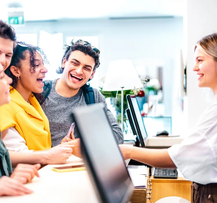 Group of smiling young adults checking in at a reception desk with a friendly receptionist.