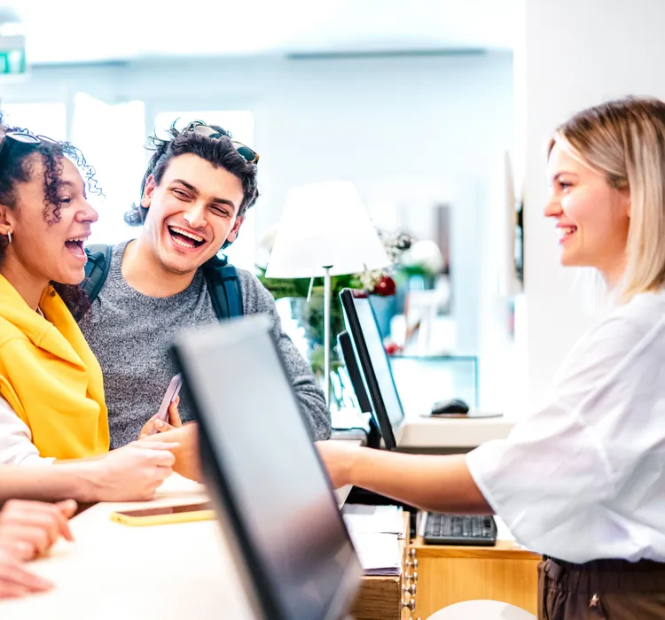 Group of smiling young adults checking in at a reception desk with a friendly receptionist.