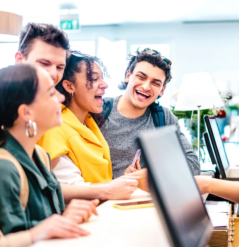Group of smiling young adults checking in at a reception desk with a friendly receptionist.