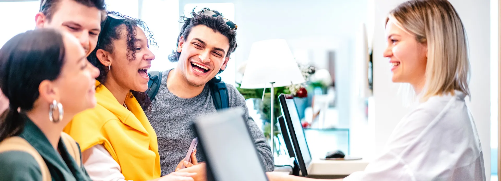 Group of smiling young adults checking in at a reception desk with a friendly receptionist.