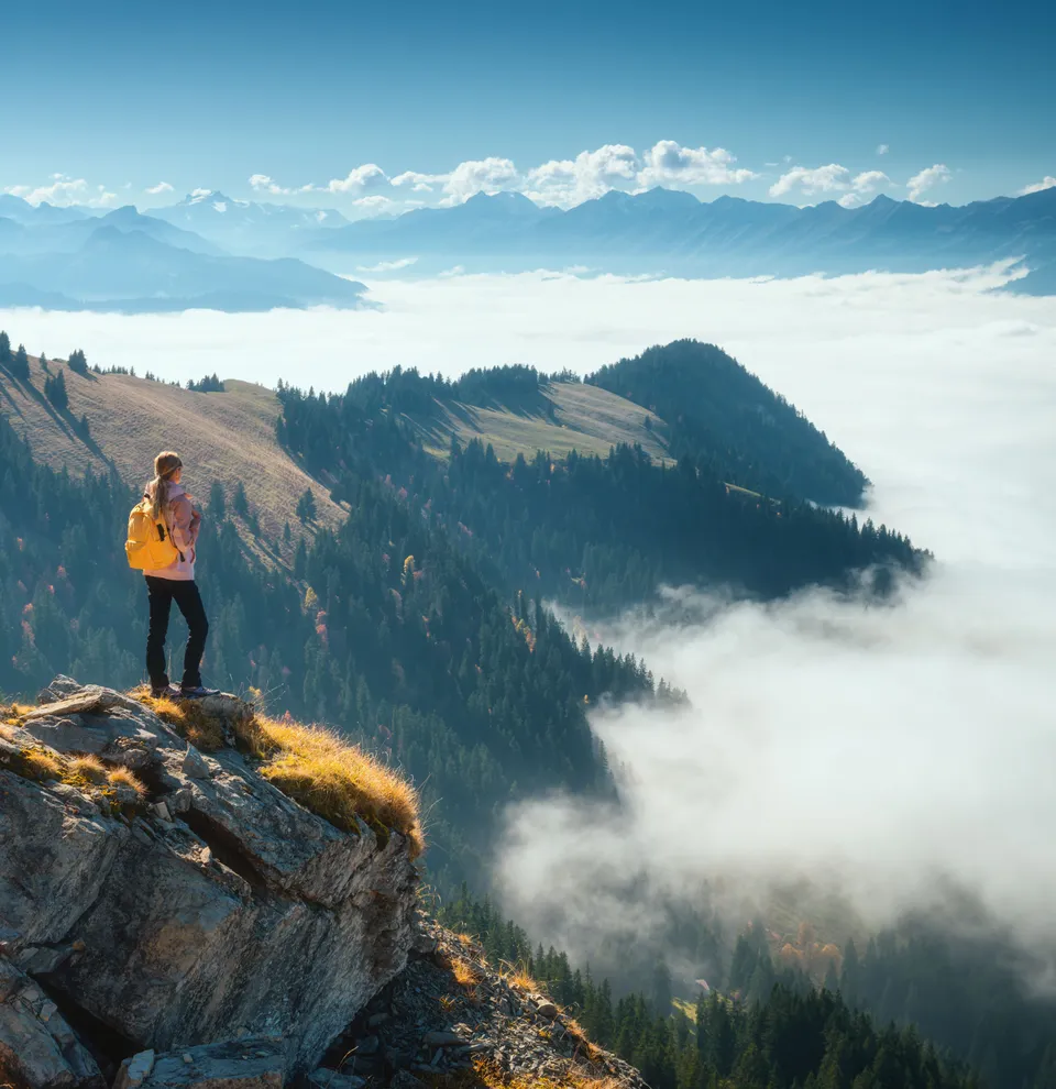Hiker with yellow backpack standing on a rocky mountain peak overlooking a misty forest landscape