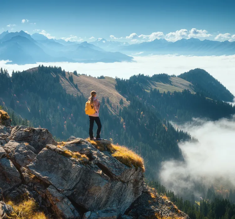 Hiker with yellow backpack standing on a rocky mountain peak overlooking a misty forest landscape