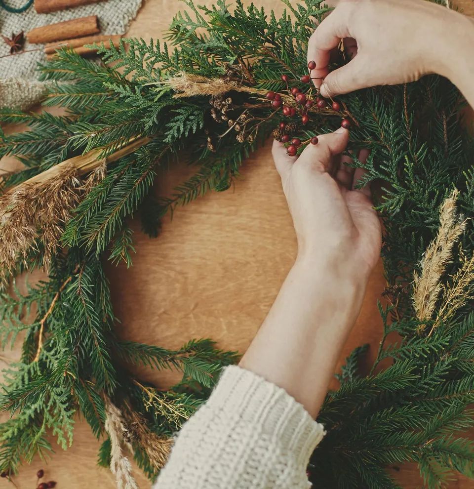 Hands decorating a homemade Christmas wreath with red berries and dried plants