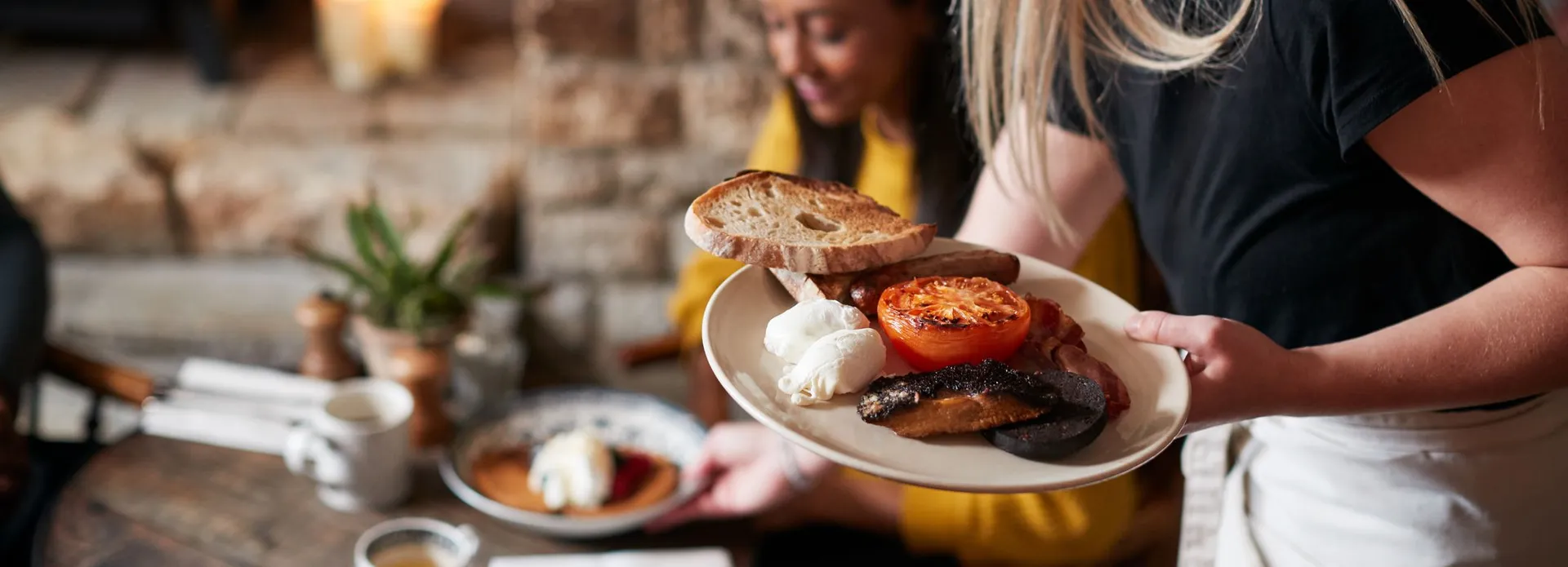 Waitress serving a plate of traditional English breakfast to a customer at a cozy restaurant