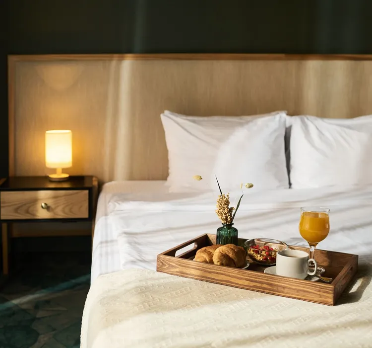 Breakfast tray with croissants, coffee, orange juice, and flowers on bed in cozy hotel room