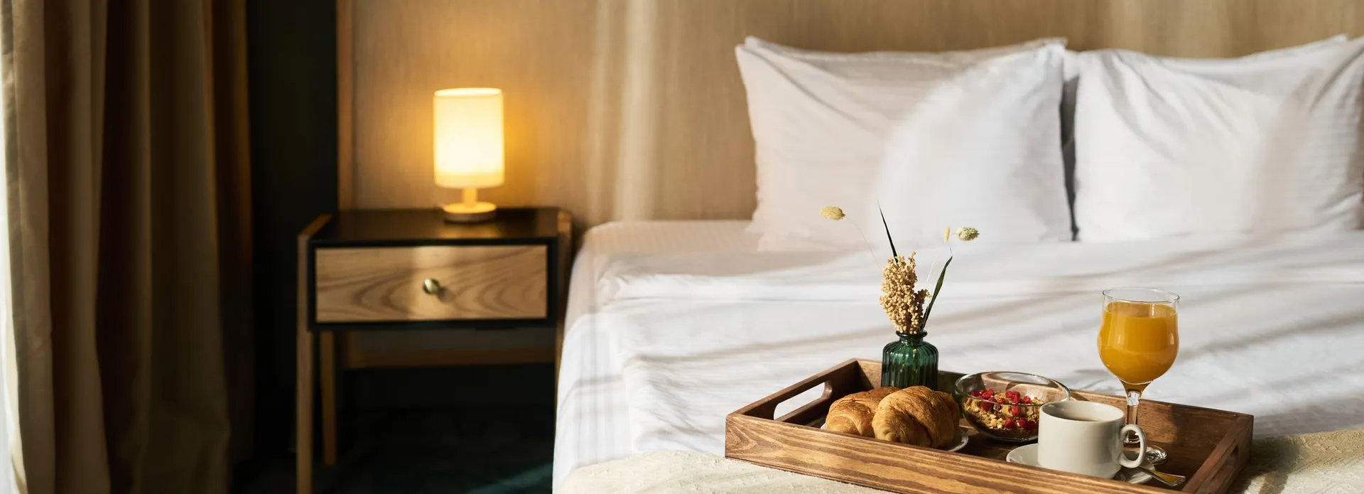 Breakfast tray with croissants, coffee, orange juice, and flowers on bed in cozy hotel room