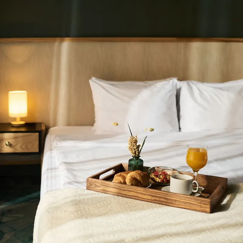 Breakfast tray with croissants, coffee, orange juice, and flowers on bed in cozy hotel room