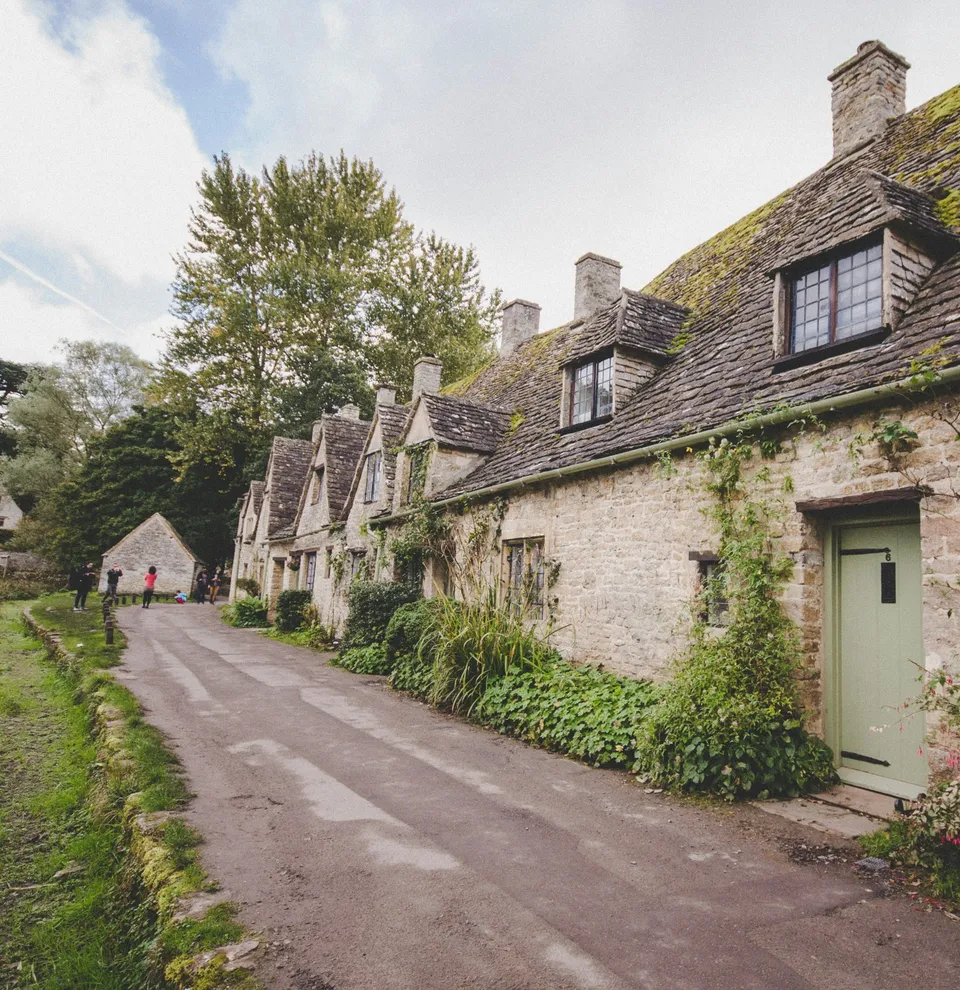 Row of charming stone cottages with mossy roofs and climbing plants in a countryside village.