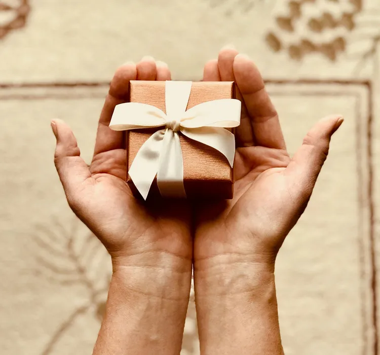 Hands holding a small gift box with a cream ribbon