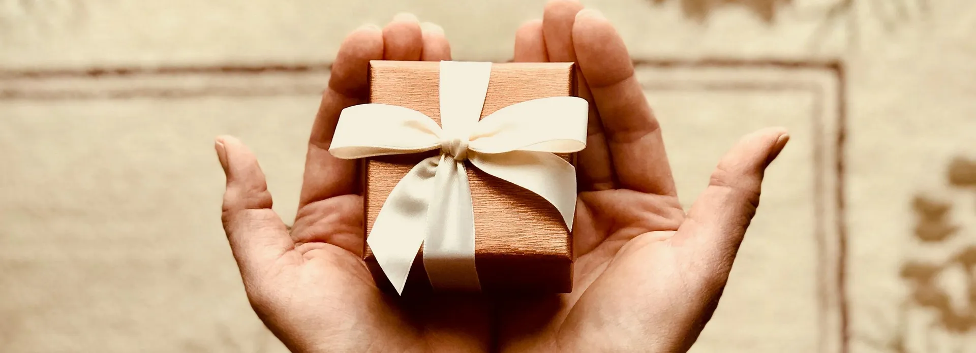 Hands holding a small gift box with a cream ribbon