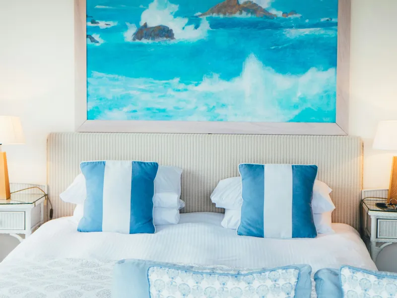 Coastal-themed bedroom with blue and white pillows and a large ocean painting above the bed