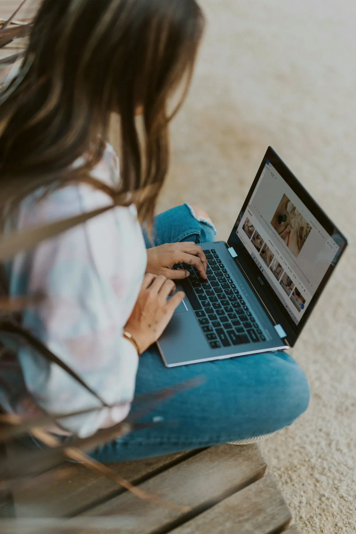 Person using a laptop outdoors, editing photos on a wooden bench