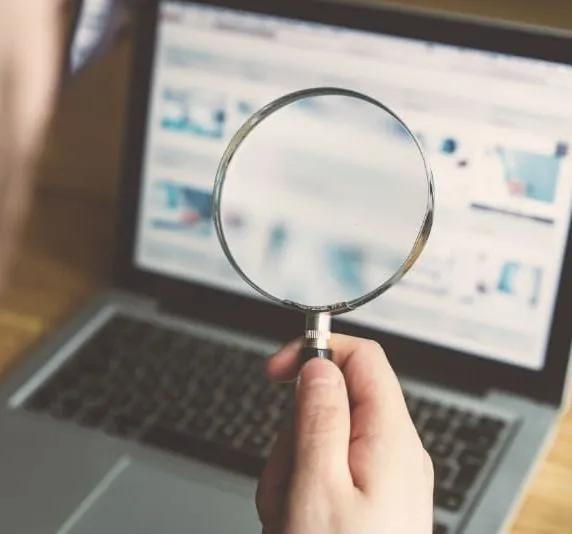 Person holding a magnifying glass in front of a laptop screen