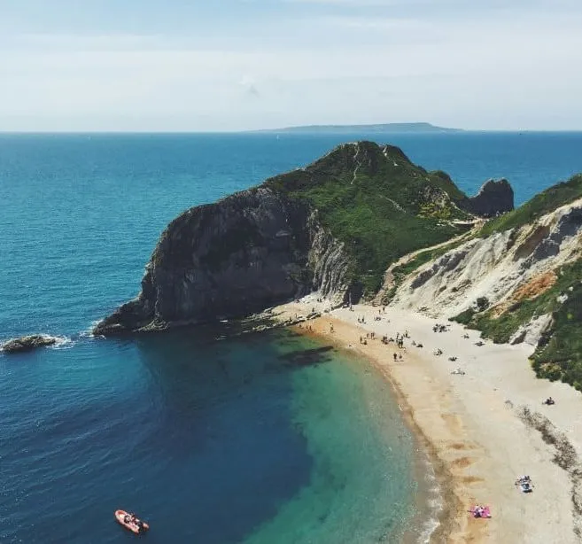 Aerial view of a coastal beach with turquoise water, cliffs, and people on the sand