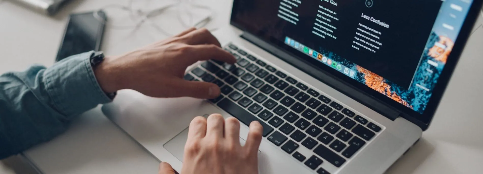 Person typing on a laptop keyboard with a phone nearby